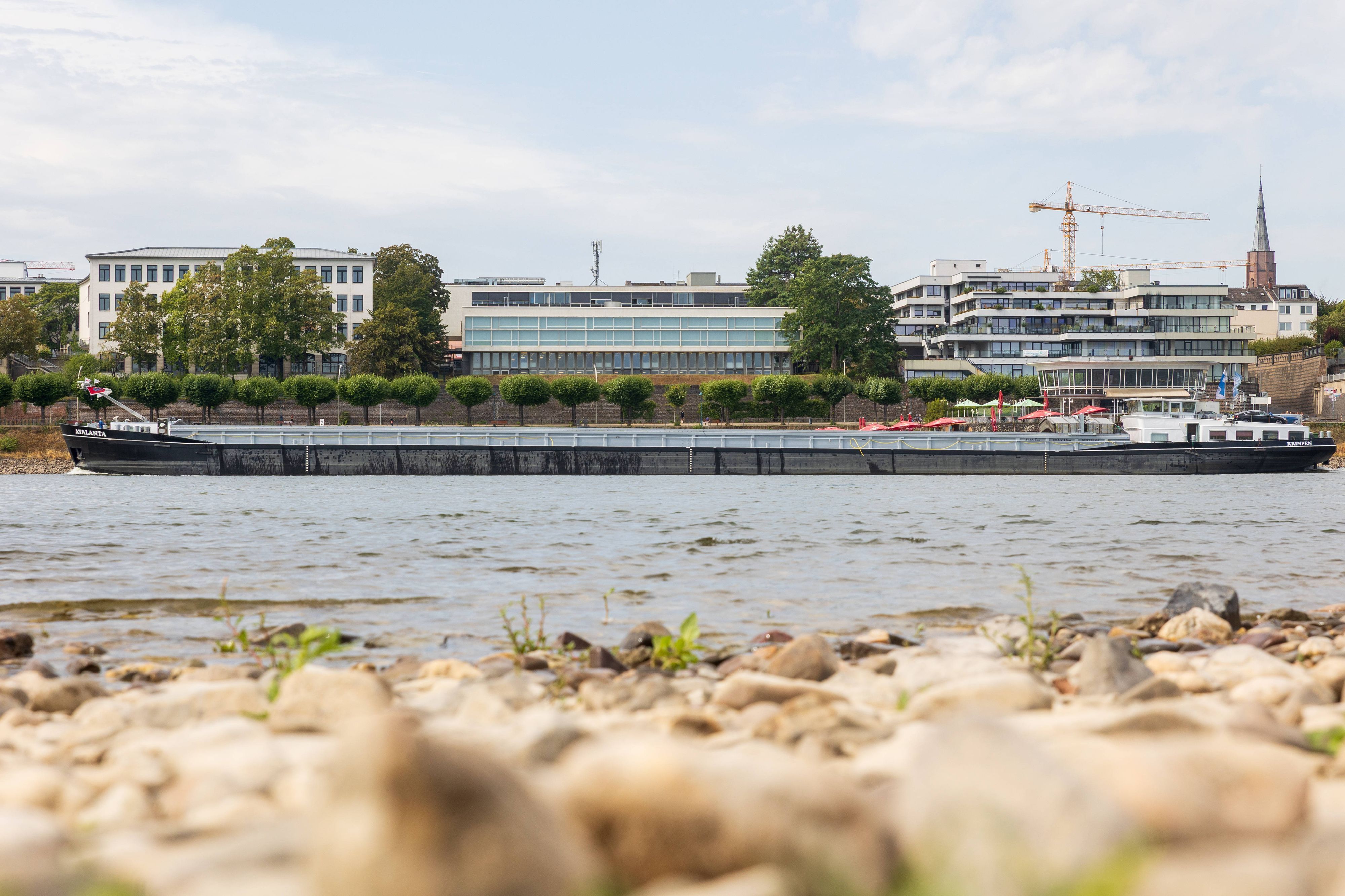 27. August 2026: Ein Binnenschiff fährt auf dem Rhein bei Bonn. Im Vordergrund sind größere Flächen aus freiliegendem Sand und Kies zu sehen, die den aktuell niedrigen Wasserstand des Flusses sichtbar machen.