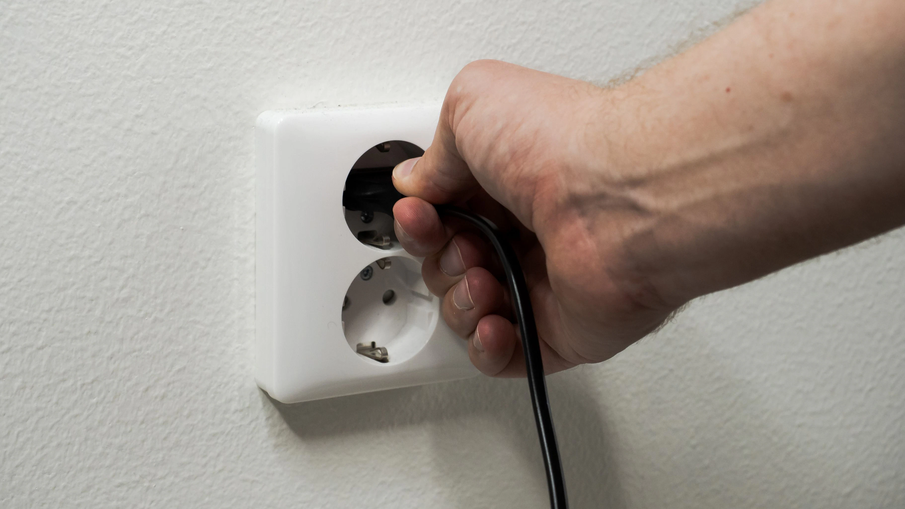 Hand plugging a black power cord into a white wall outlet. Energy, electricity and home concept.