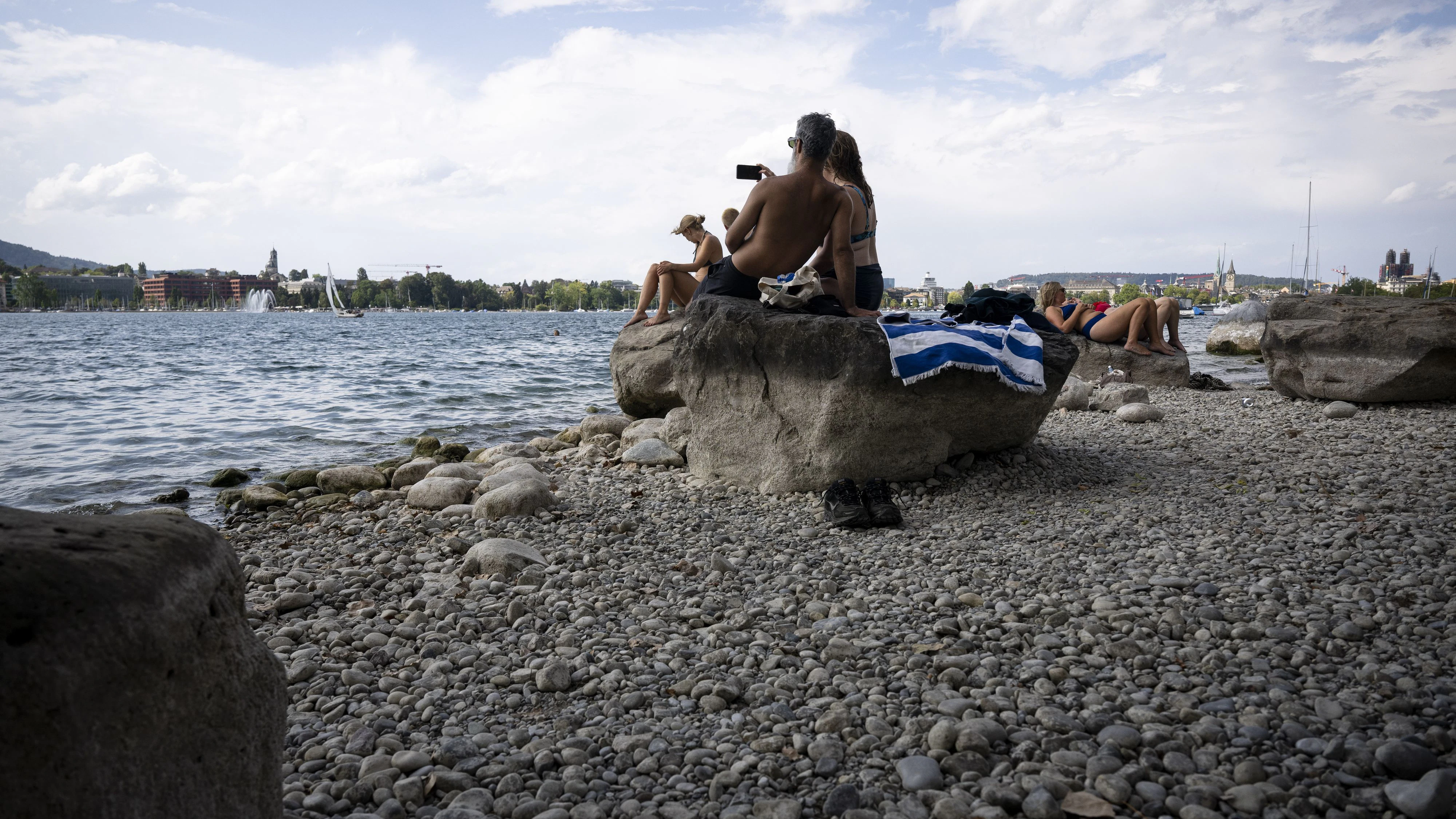 Menschen geniessen auf Steinen die Sonne am Ufer des Zürichsees. Durch die anhaltende Trockenheit hat der Pegel im August 2026 seinen 74 Jahre alten Tiefststand-Rekord gebrochen. Der Pegel an der offiziellen Messstation beim Zuerichhorn sank auf 405,45 Meter über Meer. Der bisherige Tiefstwert stammte aus dem März 1952.