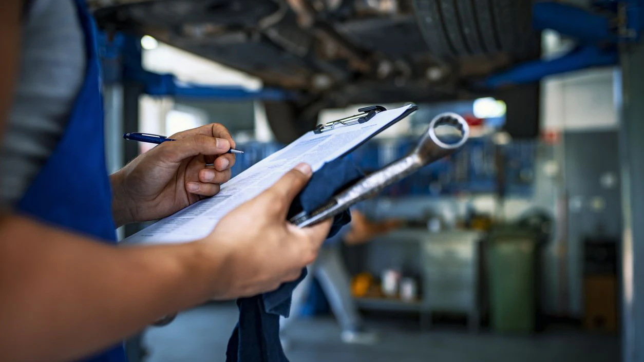 Unrecognizable Male mechanic under car preparing checklist in workshop. Photo of mechanic taking notes under a car.