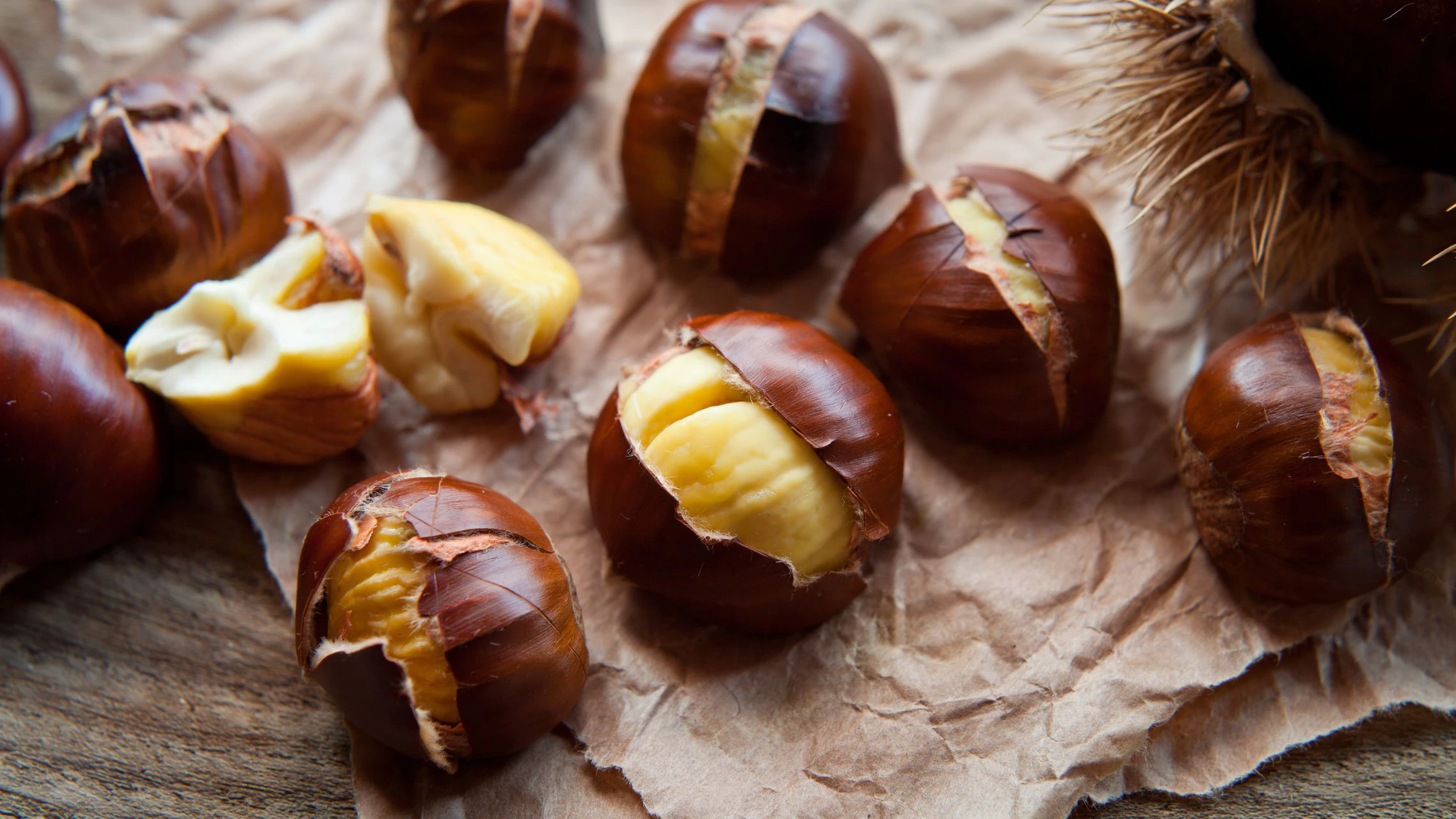 Traditional Christmas dish  - Ripe Sweet Roasted Chestnuts, cracked shells after put to the fire, natural paper and old wooden rustic background.