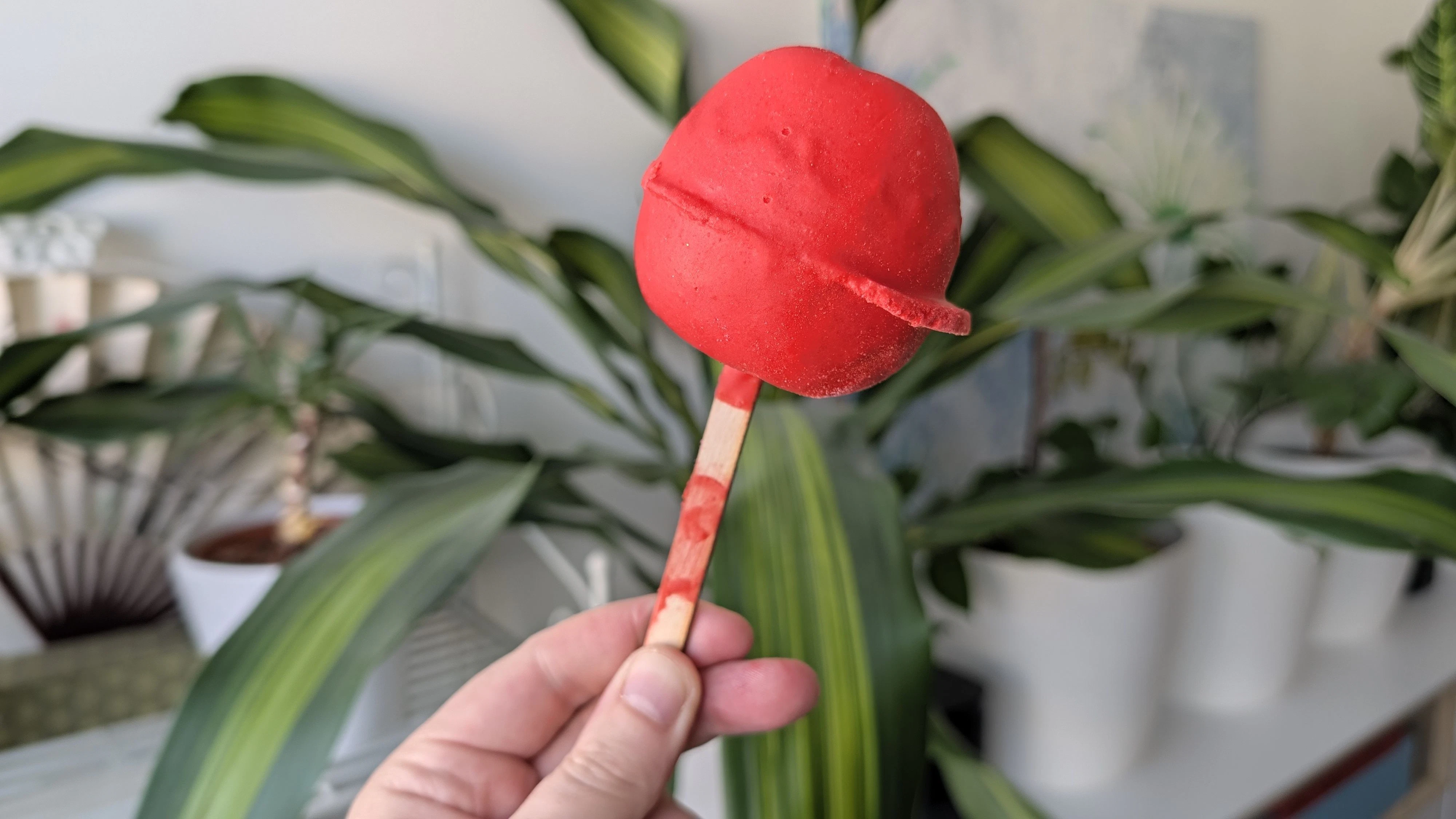 Die Badebombe Toffee Apple sieht aus wie ein roter kandierter Apfel auf einem Holzstab. 