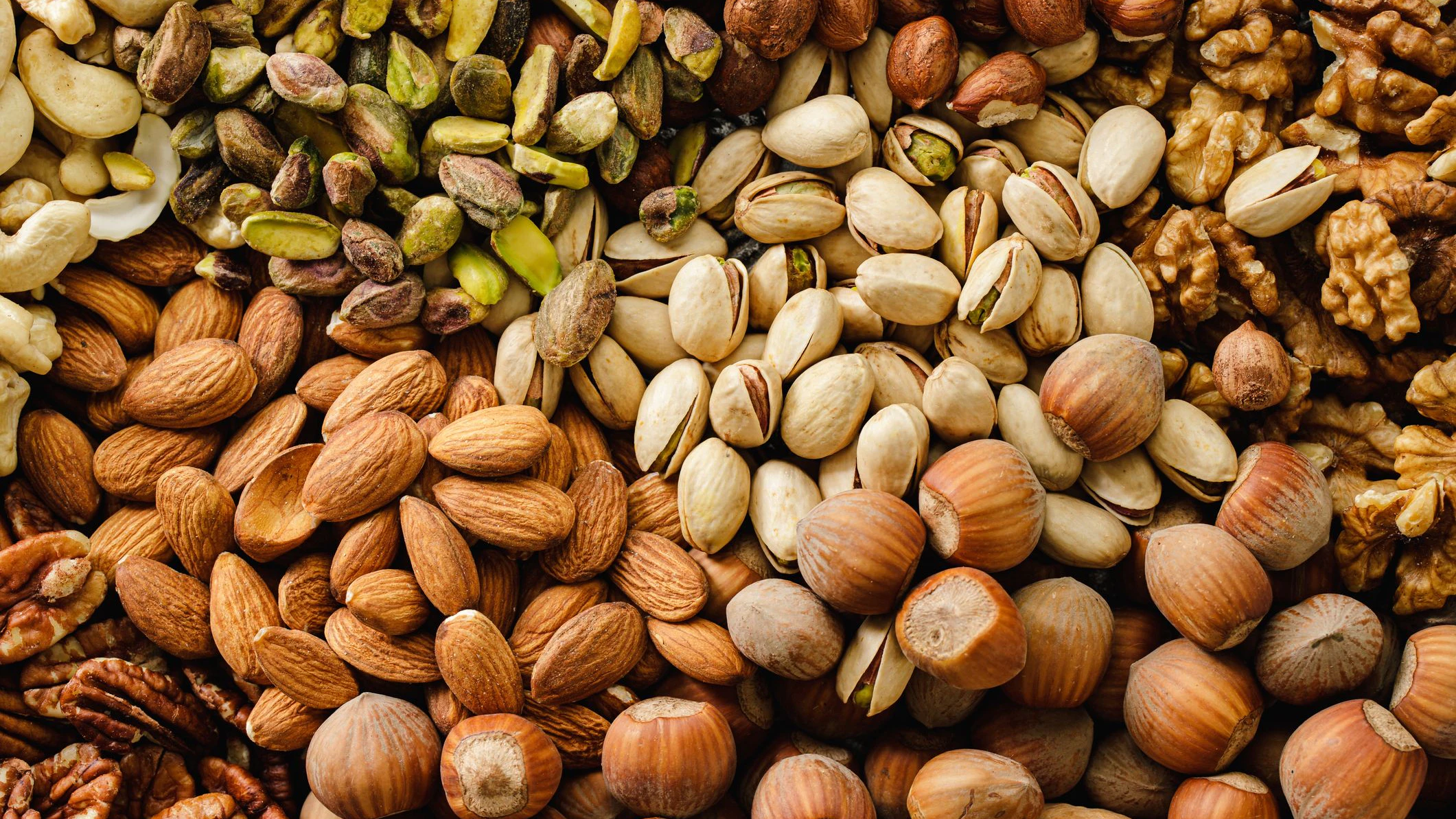 Full frame of mixed dry fruits. Top view of cashew nuts, pistachios, walnuts, hazelnuts, almons and pecan nuts heap. A vibrant assortment of mixed nuts, including almonds, pistachios, walnuts, and hazelnuts, perfect for food and nutrition-related visuals