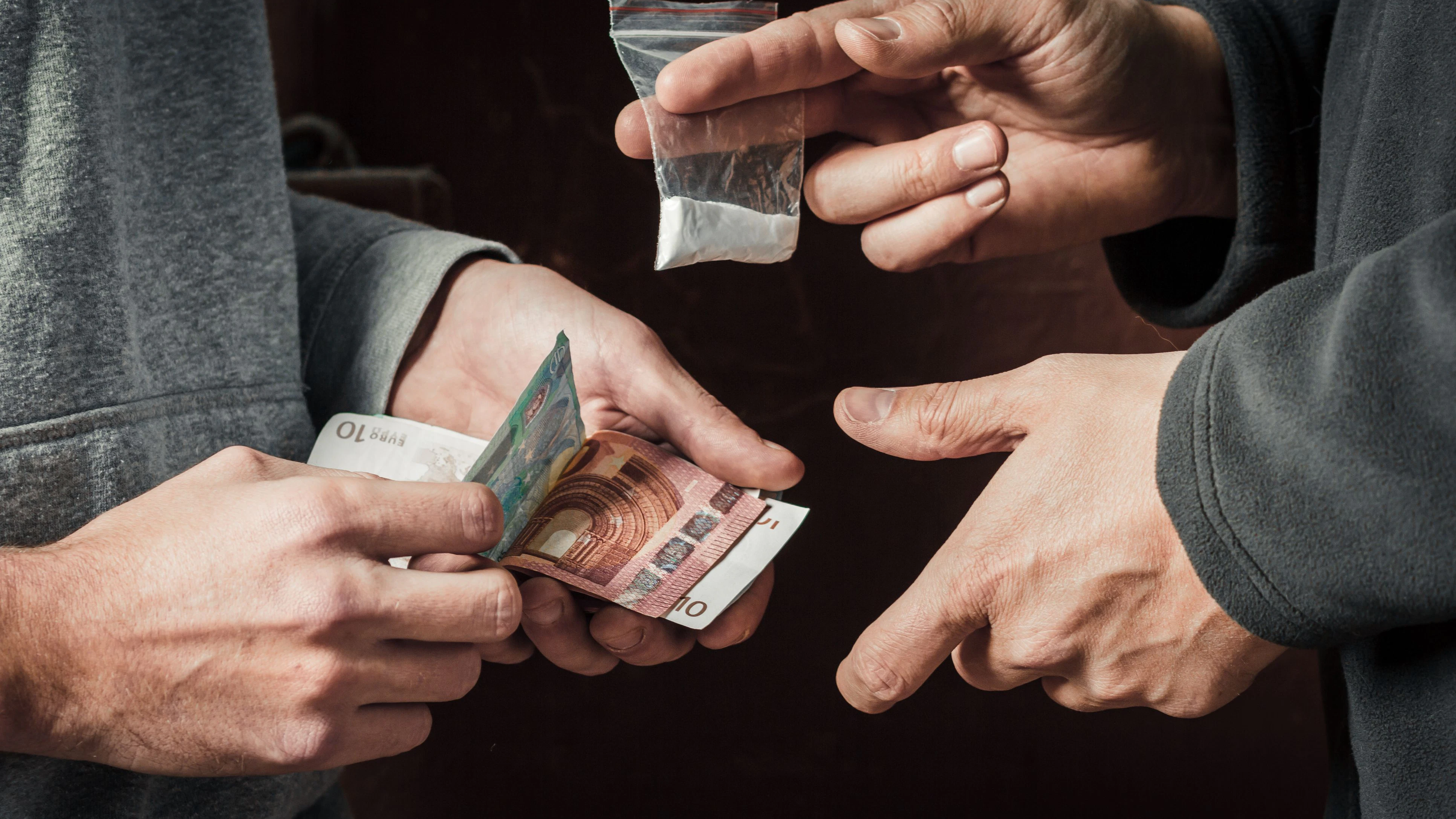 Hand of addict man with money buying dose of cocaine or heroine or another narcotic from drug dealer. Drug abuse and traffic concept.