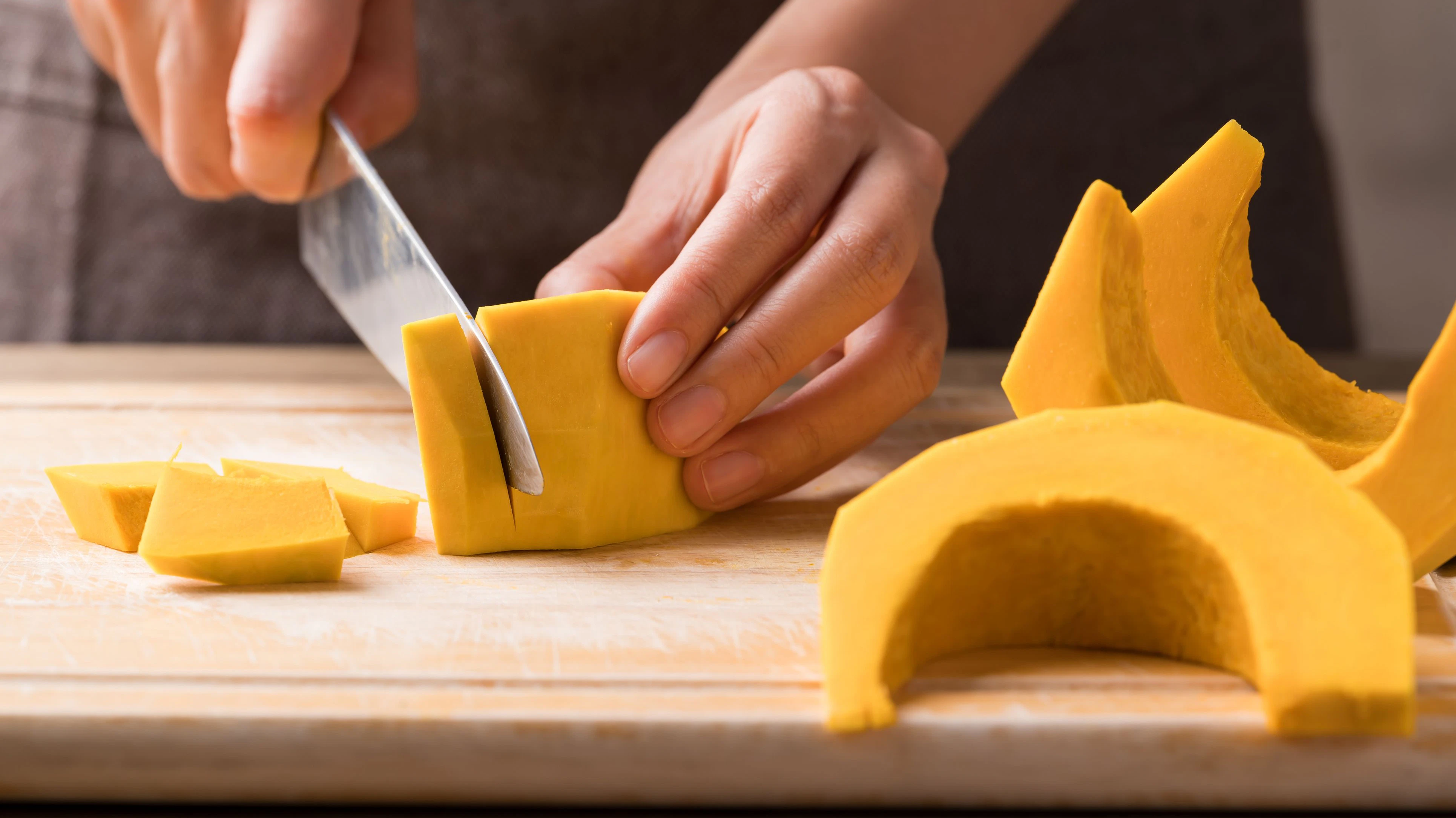 Hand holding kitchen knife and cutting pumpkin on wooden board, Homemade cooking