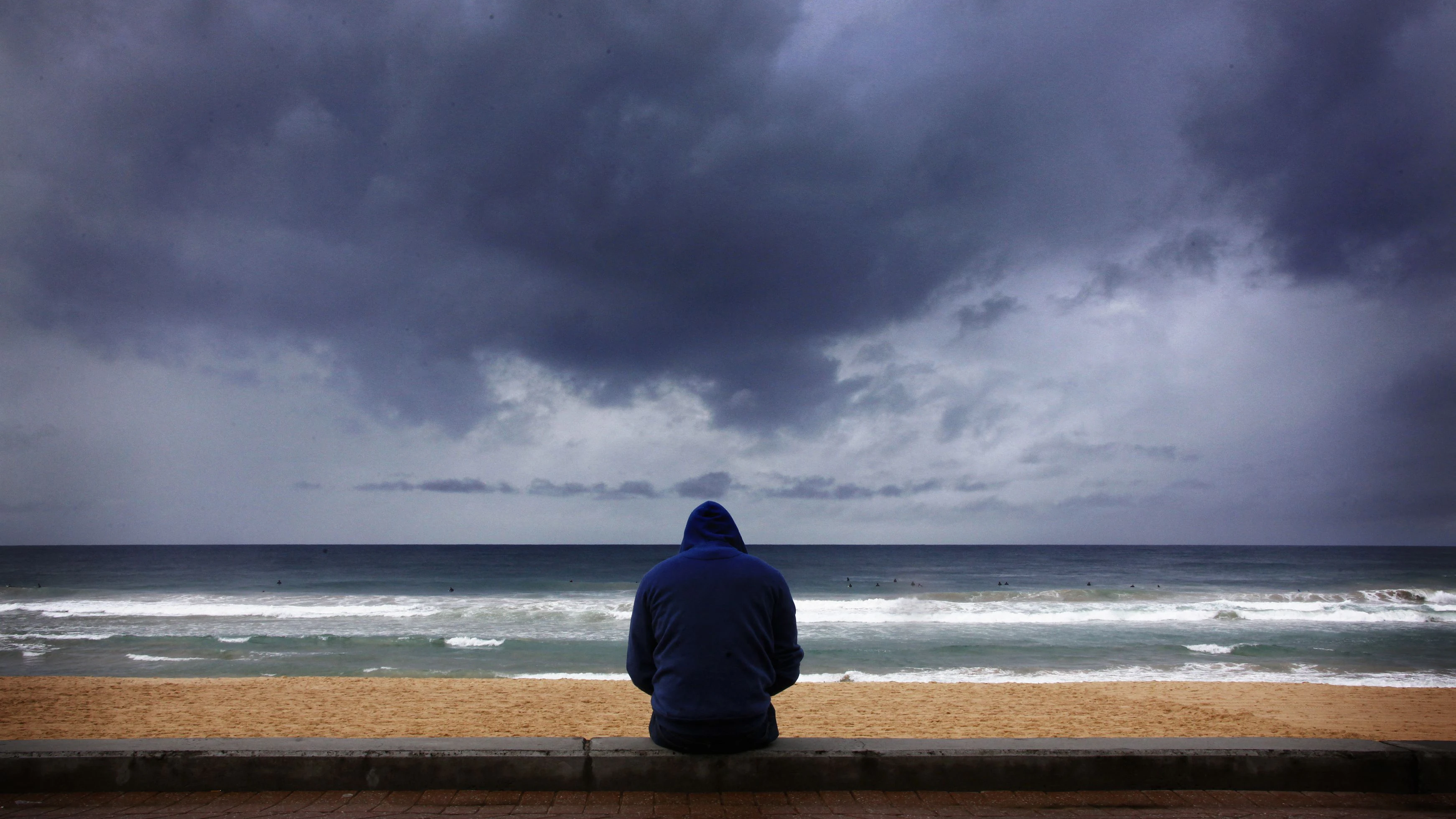 Ein Surfer beobachtet die Wellen, während sich Sturmwolken vom Pazifik her zusammenziehen 