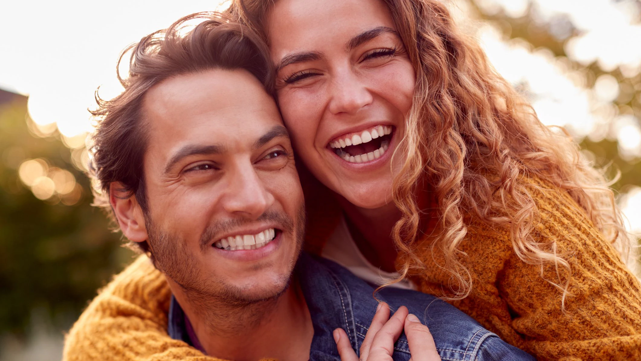 Portrait Of Happy Loving Couple With Man Giving Woman Piggyback As They Hug In Autumn Park Together