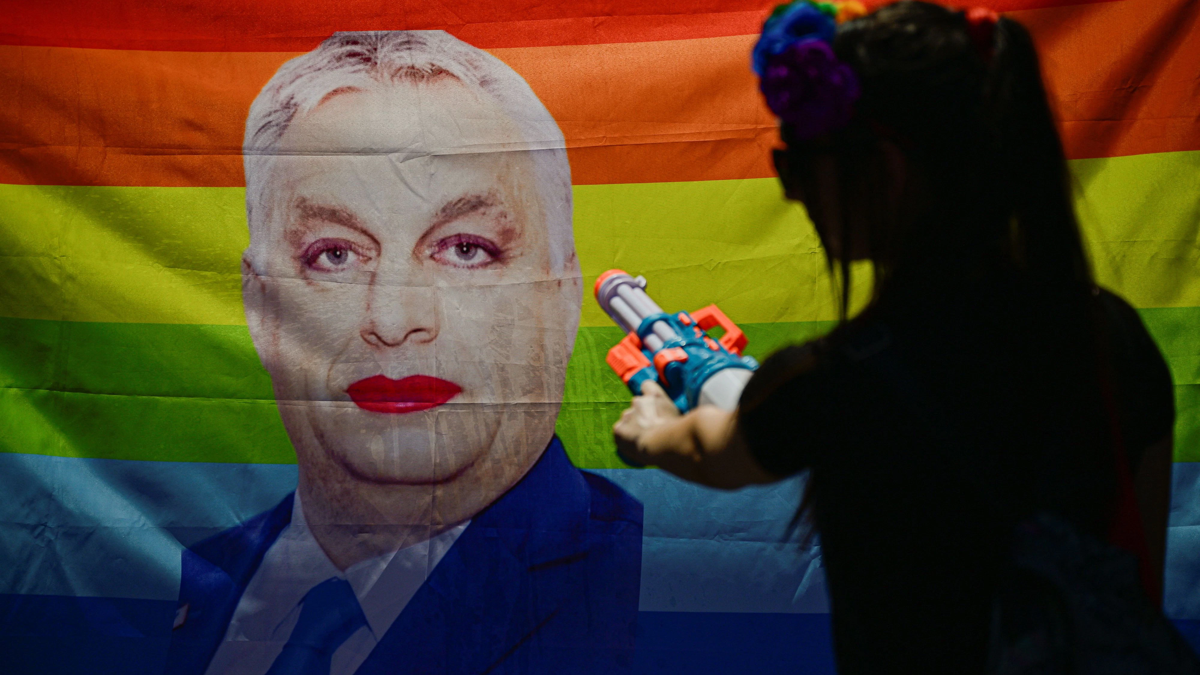 A woman holds a toy gun next to a Pride flag featuring an image of former Hungarian Prime Minister Viktor Orban wearing make-up, as people gather to attend the Budapest Pride march in Budapest, Hungary, June 27, 2026. REUTERS/Marton Monus TPX IMAGES OF THE DAY     