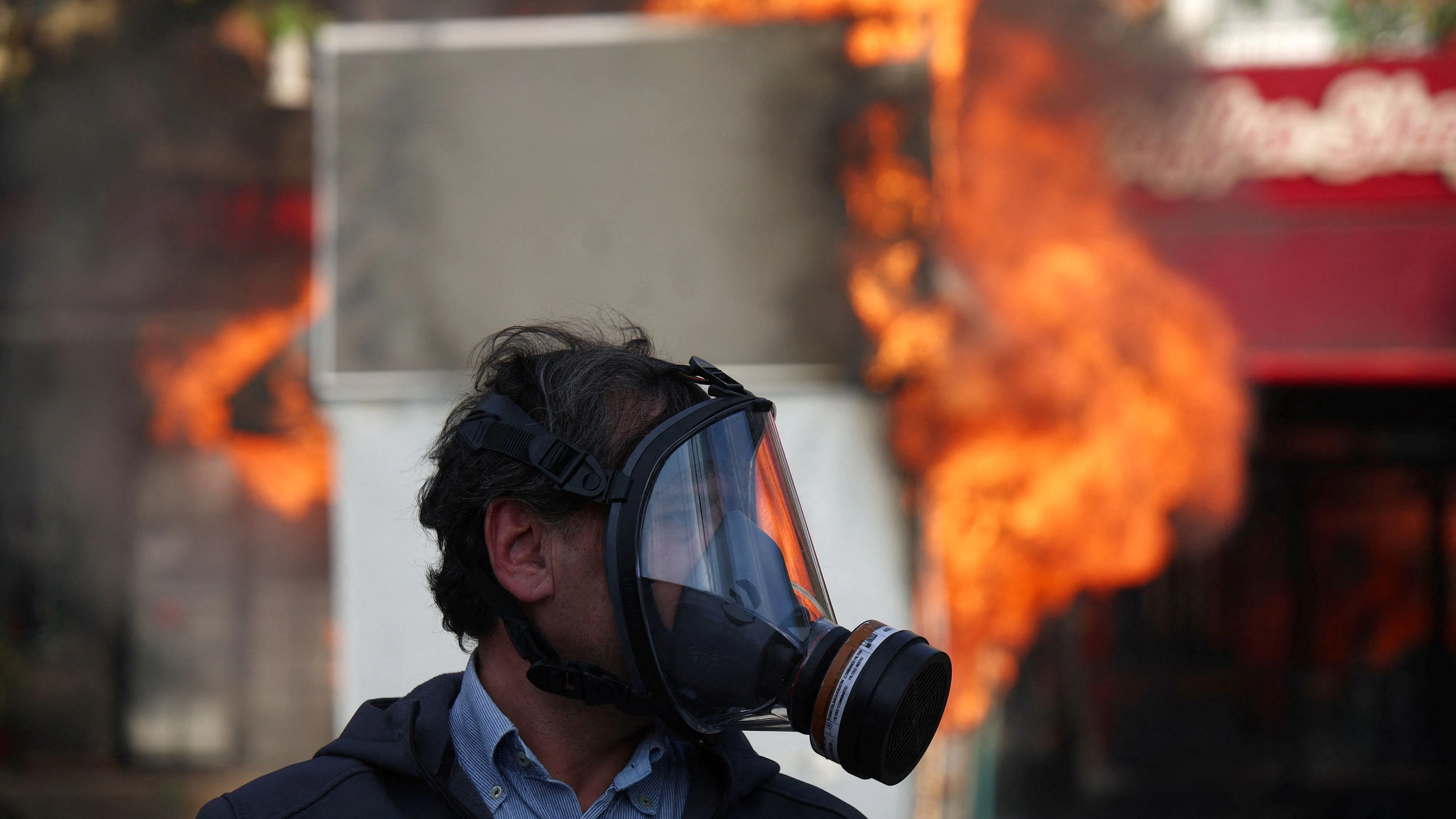 A man using a gas mask looks on near a fire during clashes between police and demonstrators amid an anti-government protest by students in Tirana, Albania, October 15, 2026. REUTERS/Florion Goga