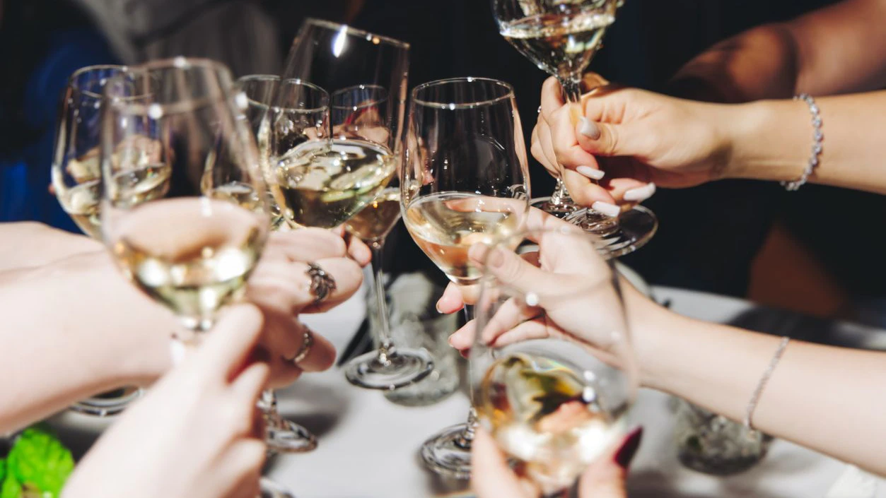 Group of guests celebrate and raise glasses, toasting and cheering with alcohol glasses with wine and champagne in the restaurant on corporate christmas birthday party event or wedding celebration