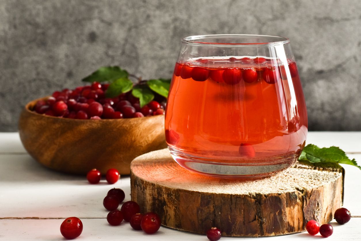 Glass Refreshing cocktail and bowl with cranberry and mint on Round wooden saw cut cylinder shape on a brown wooden table. Selective focus