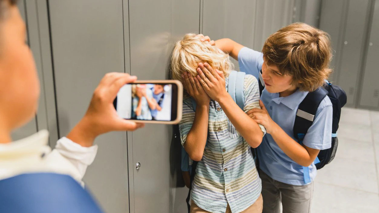 Schoolchildren cruel boys filming on the phone torturing bullying their classmate in school hall. Puberty difficult age
